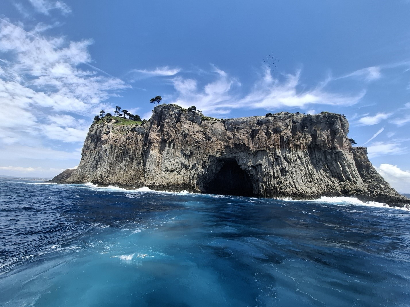 Dramatic volcanic rock island formation with sea cave rising from turquoise ocean waters off Jeju coast